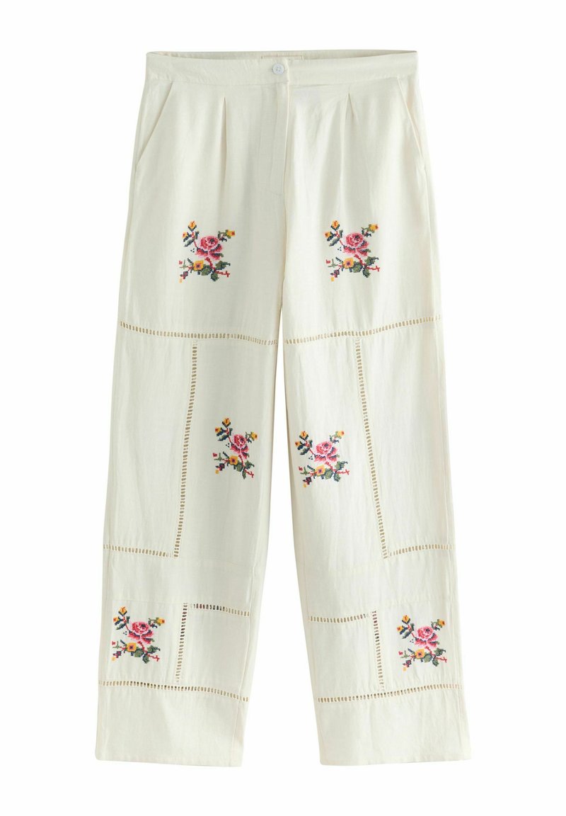 Pantaloni a gamba larga di colore crema con ricami floreali in rosa, giallo e verde. Presentano pieghe e motivi decorativi a forma di taglio lungo le cuciture.