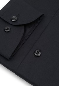 Złożony czarny rękaw i mankiet koszuli z czarnymi guzikami, ukazujący szczegółowe szycie i gładką teksturę materiału.