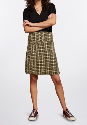 Kvinde iført sort kortærmet top, mønstret knælange nederdel med grønne og pink blomster, og mørkerøde sneakers med hvide snørebånd.