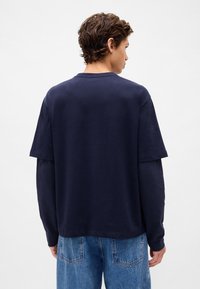 Granatowy, oversize'owy t-shirt z bawełny z krótkimi rękawami, z okrągłym dekoltem i luźnym krojem, zestawiony z jasnoniebieskimi dżinsami.