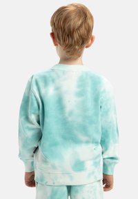 Světle modrý tie-dye svetr s žebrovanými manžetami a výstřihem, vyrobený z měkké tkaniny, se uvolněným střihem a minimálním logem.
