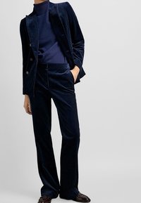 Granatowy garnitur z korduroju składający się z dopasowanej marynarki i prostych spodni, z ryżowym golfem pod spodem oraz błyszczącymi butami.