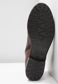 Semelle d'une botte en cuir marron avec un motif de bande de roulement en caoutchouc profond, fermeture éclair latérale et taille 37 indiquée sur la semelle.