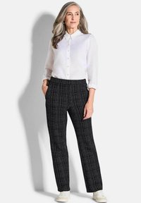 Camicia bianca con bottoni e maniche lunghe, abbinata a pantaloni neri con motivo. I pantaloni presentano un design testurizzato e tasche laterali.