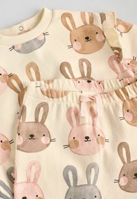 Souprava loungewear z bavlny s potiskem králičí tváře v pastelových barvách: béžová, hnědá, růžová a šedá. Obsahuje tričko a odpovídající kalhoty.