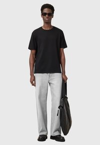 T-shirt in cotone nero, vestibilità comoda, abbinato a jeans grigi chiari e accessori neri. Il modello tiene in mano una borsa a tracolla nera e indossa occhiali da sole.