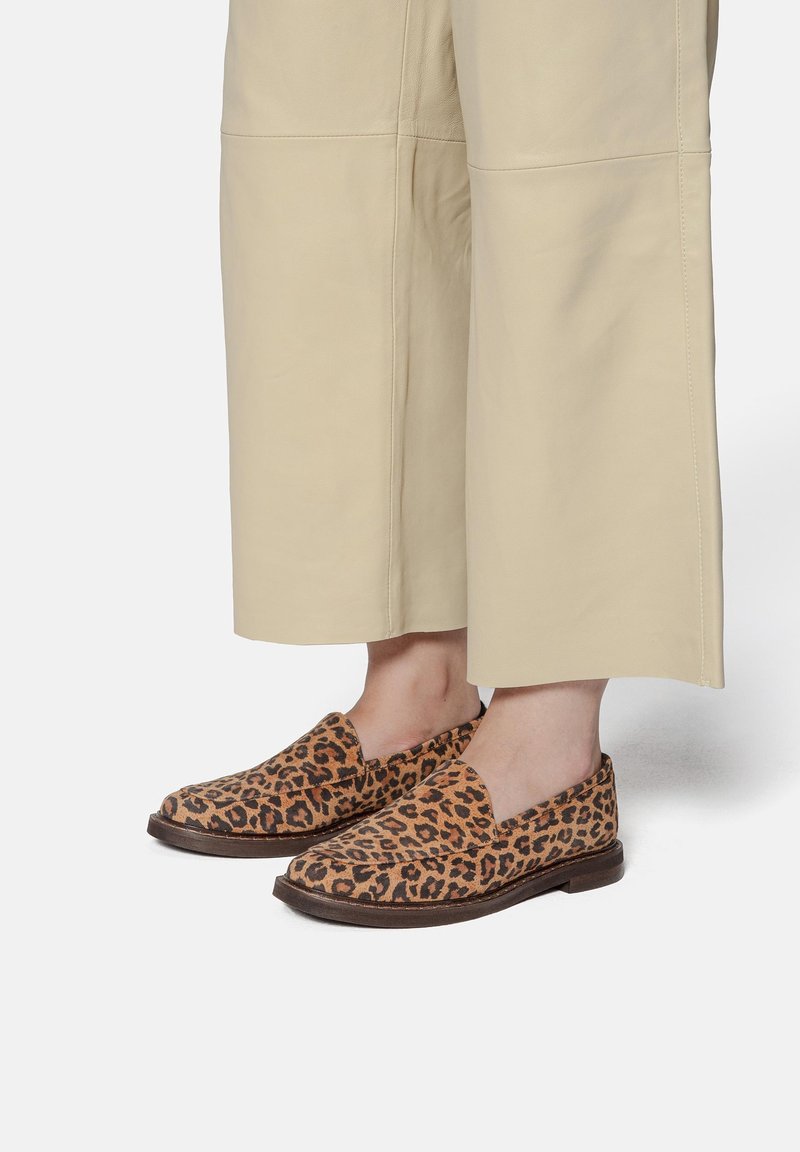 Chaussures à enfiler à imprimé léopard portées avec un pantalon beige large et court sur pieds nus.