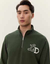 Pullover zip-up di colore verde scuro, realizzato in tessuto morbido, con il logo 'LD' bianco sulla zona sinistra del petto. Il colletto è alto e strutturato.