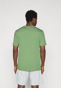 Grünes Baumwoll-T-Shirt mit Rundhalsausschnitt und kurzen Ärmeln, das eine glatte Textur und eine lockere Passform aufweist, kombiniert mit hellgrauen Shorts.