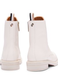 Botines de piel blanca con textura suave, puntera redonda, detalle de cremallera y tiradores en contraste; logo grabado en el talón.