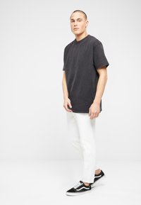 Camiseta de algodón negra de manga corta, cuello redondo, ajuste relajado, combinada con jeans blancos ajustados y zapatillas negras con acentos blancos.