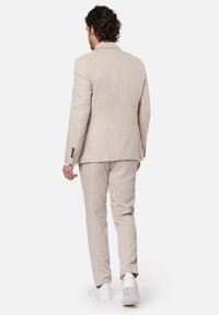 Beżowy garnitur z lnu o dopasowanym kroju, z marynarką z jednym rozcięciem, dopasowanymi spodniami i białymi sneakersami. Gładka tekstura z subtelnym splotem.