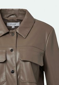 Braune Lederjacke mit klassischem Kragen, Druckknöpfen, zwei Brusttaschen und glatter Textur. Herstelleretikett innen sichtbar.