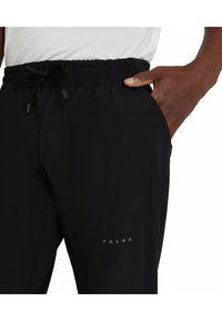 Zwarte sportbroek met een elastische tailleband, trekkoordverstelling en zijzakken. Heeft een subtiele logo op het bovenbeen.