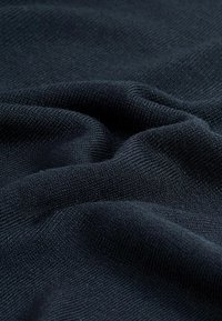 Gros plan d'un tissu tricoté bleu marine foncé avec une texture fine côtelée visible et des plis doux.