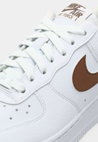 Bijeli kožni Nike Air Force 1 tenisači s bijelim vezicama i smeškim Nike swoosh logom sa strane, izbliza.