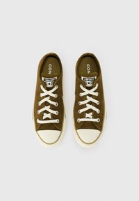 Zapatillas de ante marrón de corte bajo con cordones blancos, puntera de goma y un parche de logo en la lengüeta. Diseño clásico con acabado texturizado.