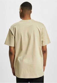 Lys beige t-skjorte med korte ermer og rund hals, laget av myk bomull, med en avslappet passform og ensfarget tekstur, vist fra baksiden.