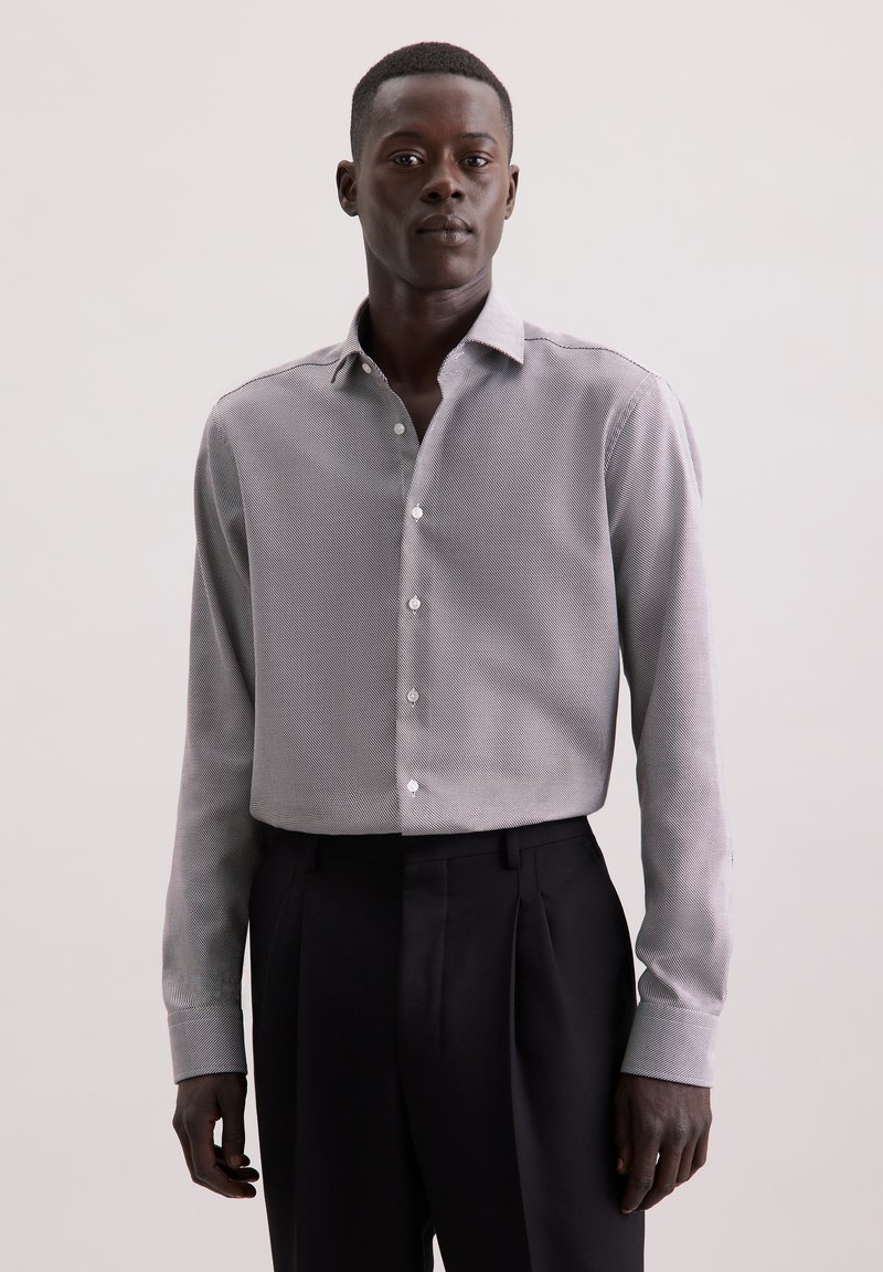 Camicia button-up grigia a motivo, con colletto classico, maniche lunghe e una texture liscia, abbinata a pantaloni sartoriali scuri.