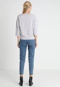 Grijze driekwart mouw top, gecombineerd met lichtblauwe jeans, met een ontspannen pasvorm en zwarte enkellaarsjes met een ritsdetail.