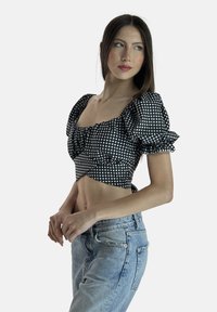 Schwarz-weiß kariertes Crop-Top mit gepufften Ärmeln, quadratischem Ausschnitt und gerafftem Vorderteil. Kombiniert mit hellblauen Jeans.