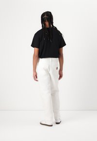 Sort kortærmet t-shirt, hvide lige bukser og hvide sneakers. Struktureret stof og synlige sømme på bukserne.