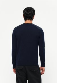 Jersey de marina hecho de tejido de punto, con mangas largas, un cuello redondo y acentos en gris contrastantes en los hombros.