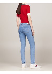 Top corto rojo de manga corta con puños a rayas blancas, combinado con jeans ajustados azul claro y zapatillas blancas con un detalle de logo en rojo, azul y blanco.