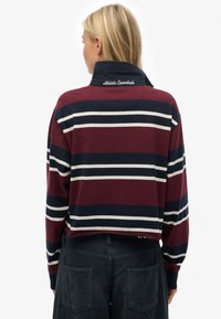Chemise à manches longues rayée bordeaux et marine avec un col, ornée de la broderie "Athletic Essentials" dans le dos.