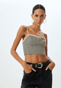 Gråternet cropped top med blondedetaljer, tynde stropper og rynkede elementer, parret med højtaljede mørke jeans og et dekorativt bælte.