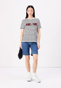 Stripet t-skjorte med korte ermer i svart og hvitt med rød "AMOUR" tekst, parret med blå denimshorts og hvite høye sneakers.
