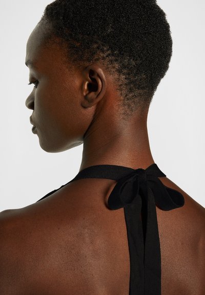 Top preto de alças com um detalhe de laço nas costas. Textura suave e design ajustado, com foco no decote e nos ombros.