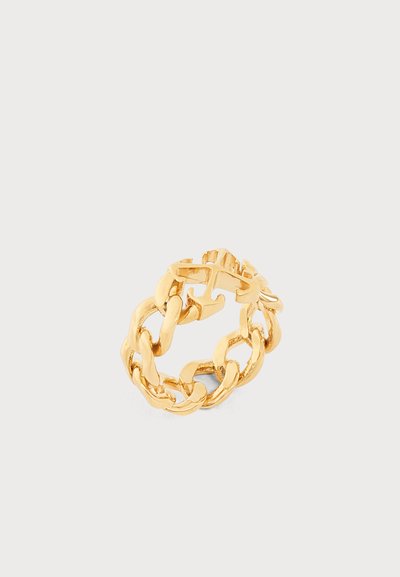 Bague en maillons de chaîne en or avec des maillons épais entrelacés et un petit détail de fermoir sur un fond clair uni.