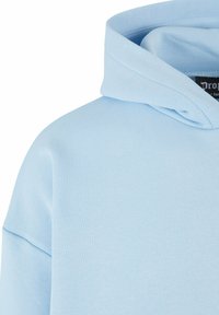 Vaaleansininen huppari, jossa on pehmeä tekstuuri, kiristettävä huppu ja hieman ylisuuri istuvuus, sekä minimimäärä ompeluyksityiskohtia.