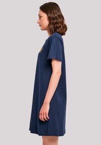 Navyblauwe T-shirt jurk met korte mouwen en een ontspannen pasvorm, voorzien van een decoratieve gele bloemenborduring op de borst. Zachte katoenmateriaal.