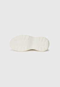 Kremfarget sneakersåle med et teksturert mønster, som har rillede seksjoner og merke detaljer, designet for grep og slitestyrke.