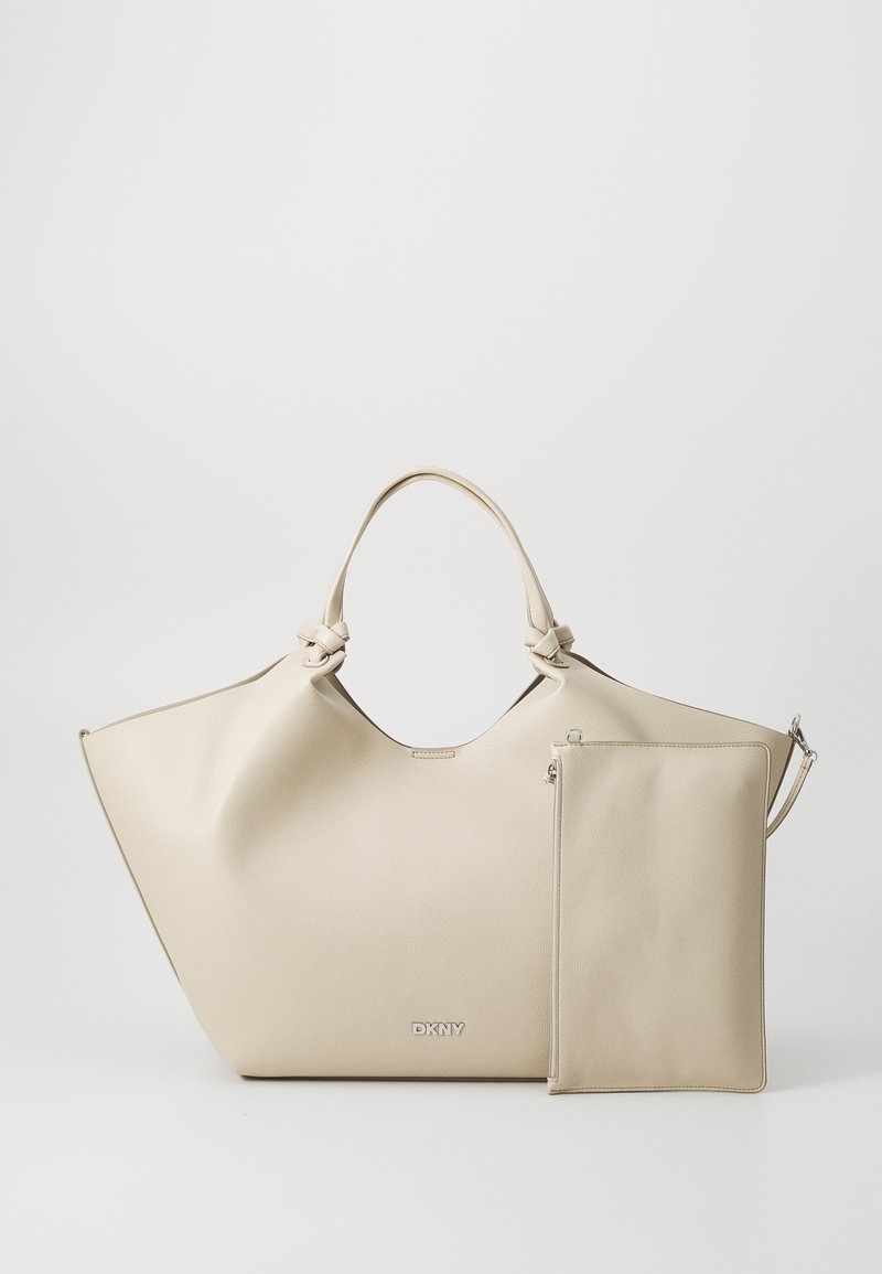 Beige tote bag med en glatt tekstur og vinklet design, som har knyttede håndtak og en avtakbar glidelåslomme. Logoen er vist på forsiden.