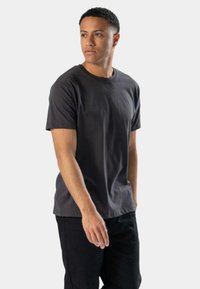 Mørkegrå bomulds t-shirt med korte ærmer, rund halsudskæring og en afslappet pasform. Kombineret med sorte bukser. Glat tekstur, minimalistisk design.