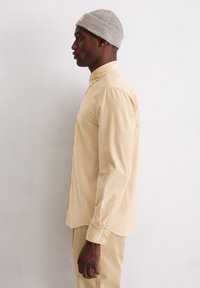 Chemise en velours côtelé beige clair à manches longues, col boutonné et tissu texturé, assortie à un bonnet gris à côtes.