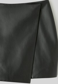 Mini-jupe en simili cuir noir à la texture lisse, présentant un design asymétrique et une silhouette épurée et moderne.