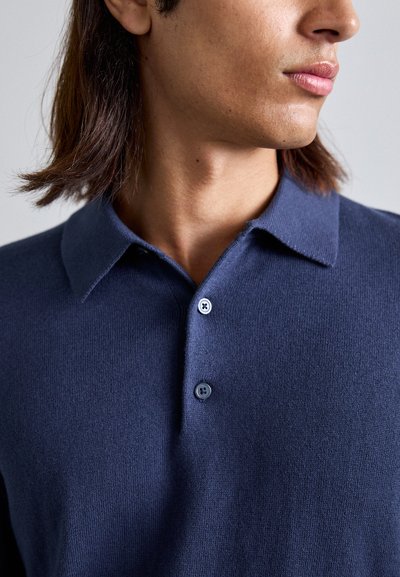 Navy knitted polo shirt with a classic collar, featuring three buttons and a smooth texture. Close-up of collar and button detail.