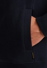 Sudadera azul marino con un bolsillo, dobladillo y puños acanalados. Cuenta con una etiqueta cosida en el lado que dice "PRIME LEGEND."