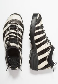 Zapatos a rayas de cebra en blanco y negro hechos de material texturizado. Cuentan con una suela de goma negra y diseño con cordones y cuello acolchado.