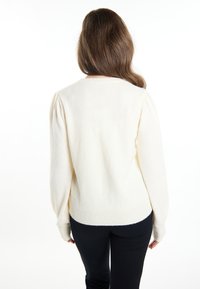 Pulover de culoare crem, cu decolteu rotund, croială lejeră și mâneci bufante. Textura moale și tivul ribborat adaugă detalii. Purtați cu pantaloni negri.