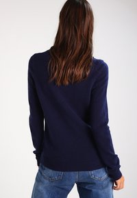 Pull en tricot bleu marine avec un col rond et des manches longues. Texture douce avec des poignets et un ourlet côtelés. Porté avec un jean en denim clair.
