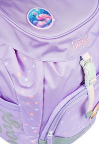 Zaino in tessuto viola con un patch rotondo a forma di fenicottero, motivi a pois pastello e una tracolla regolabile con un accento grigio.
