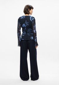 Blouse en bleu transparent avec des motifs d'étoiles et de lune, taille cintrée, manches longues ; associée à un pantalon à pinstripes bleu marine taille haute.