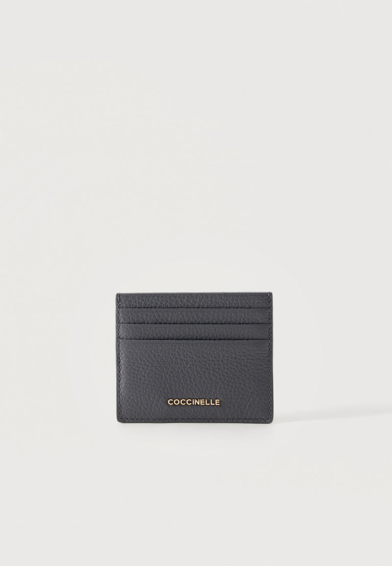 Porte-cartes en cuir noir texturé avec quatre emplacements pour cartes et logo doré "COCCINELLE" à l'avant, présenté sur fond blanc.
