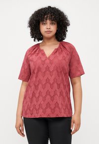 Blusa corta di colore ruggine con scollatura a V, caratterizzata da un motivo geometrico testurizzato e dettagli arricciati al collo.