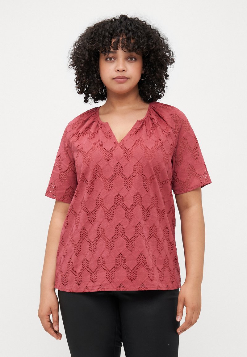 Blusa corta di colore ruggine con scollatura a V, caratterizzata da un motivo geometrico testurizzato e dettagli arricciati al collo.